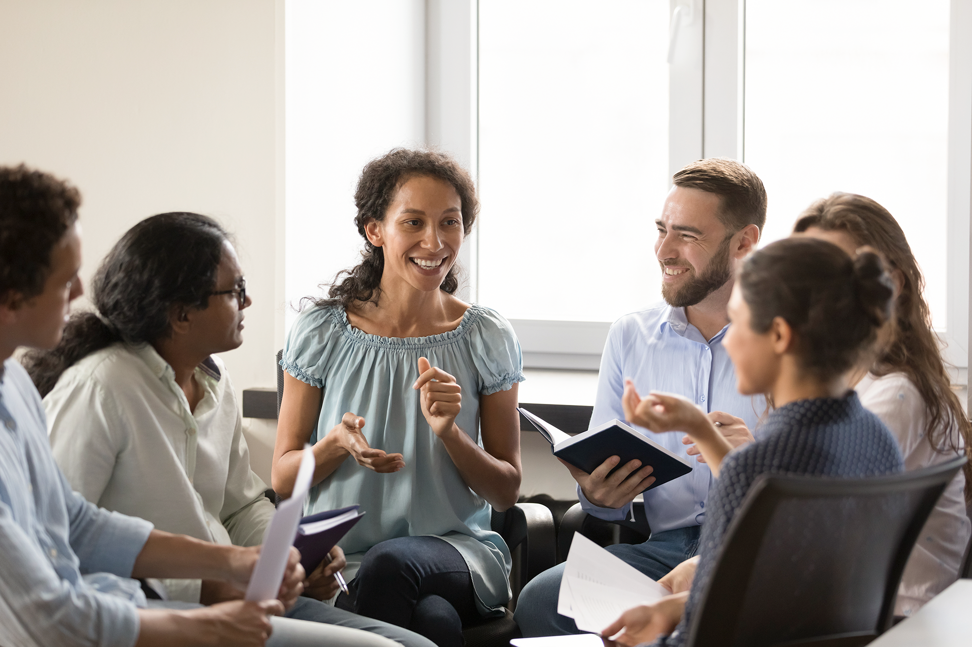 AdobeStock_529821089 Group of six people discussing ideas with notebooks in hand.